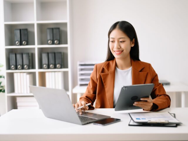 Successful,Asian,Businesswoman,Analyzing,Finance,On,Tablet,And,Laptop,At