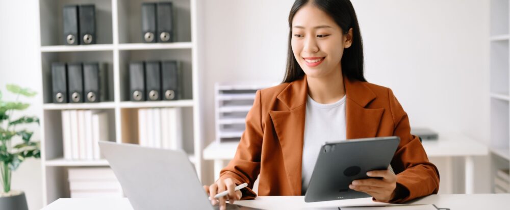 Successful,Asian,Businesswoman,Analyzing,Finance,On,Tablet,And,Laptop,At